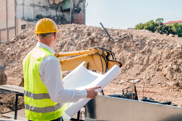 Portrait of site manager posing with blueprints against unfinished building