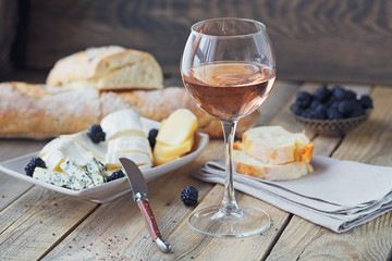 A glass of rose wine served with cheese plate, blackberries and baguette