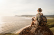 © soft_light - Woman traveller with backpack and binoculars in hands enjoying view coast on sunset