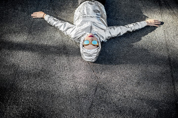 Lifestyle portrait of a modern woman in silver jacket with hood and sunglasses lying outdoors on the asphalt road