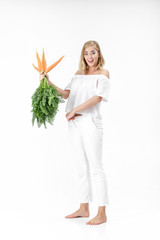 Wall Mural - blond woman holding fresh carrot with green leaves on white background. girl eats carrots and grows thin