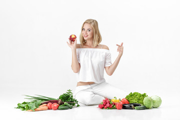 Canvas Print - Beautiful blond woman in white clothes and lots of fresh vegetables on white background. girl is eating nectarine