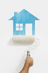 Wall Mural - paint roller hand with blue house symbol painting on wall isolated on white