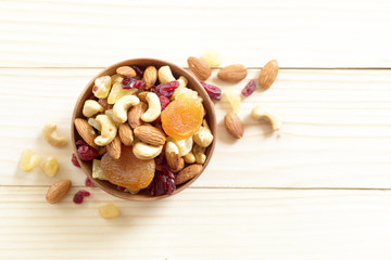 Poster - mixed nuts and dried fruit in wooden bowl on wooden table top view. Walnut, pistachio, almond, hazelnut, cashews, apricot, berry, banana, pineapple, Healthy food and snack