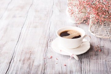 White cup of coffee with pink flowers on old white wooden background with copy space.