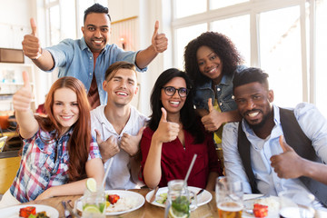 Canvas Print - happy friends showing thumbs up at restaurant