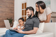 © LIGHTFIELD STUDIOS - multiethnic family sitting on sofa and using laptop together