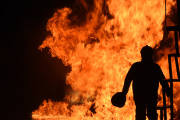 Silhouette of Firemen fighting a raging fire with huge flames of burning timber