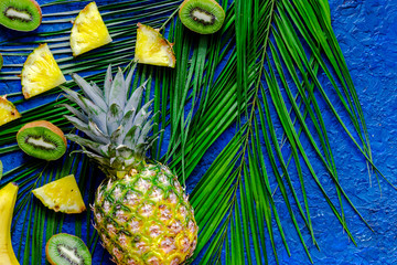  Koncepcja letnich owoców tropikalnych. Kiwi, ananasa i palmy gałąź na błękita stołu tła odgórnym widoku