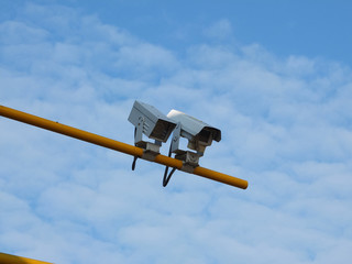 two security cameras on yellow pole with blue sky background