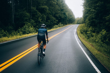 Selective focus shot of professional road cyclist riding down wet and windy mountain road in forest, on aero road bike from carbon