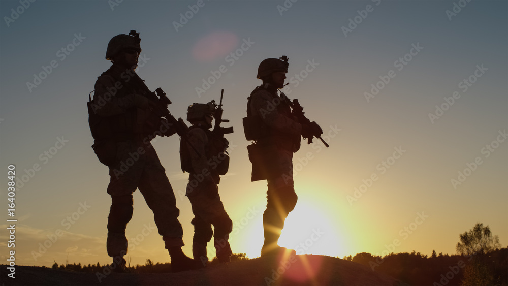 Squad of Three Fully Equipped and Armed Soldiers Standing on Hill in Desert Environment in Sunset Light. - obrazy, fototapety, plakaty 