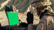 Soldier is Using Laptop Computer with Green Screen and Radio for Communication During Military Operation in the Desert.
