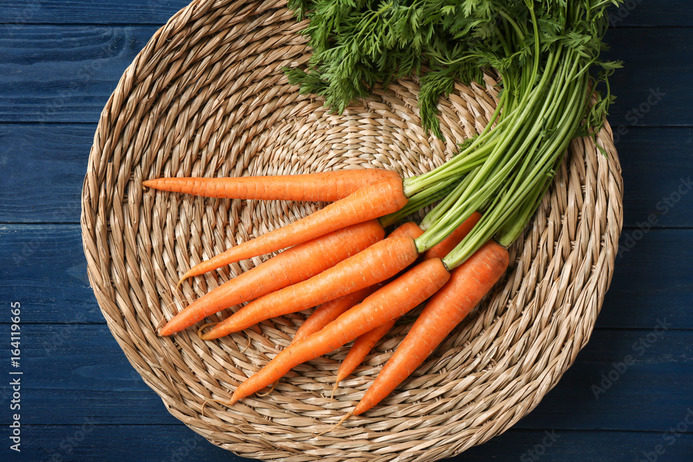 Organic raw carrots on wicker plate against color background