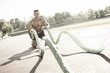 © Addoro - Handsome middle aged man working out on a running track. Healthy adult man doing battle rope exercise. Tanned skin and shirtless middle-aged man.