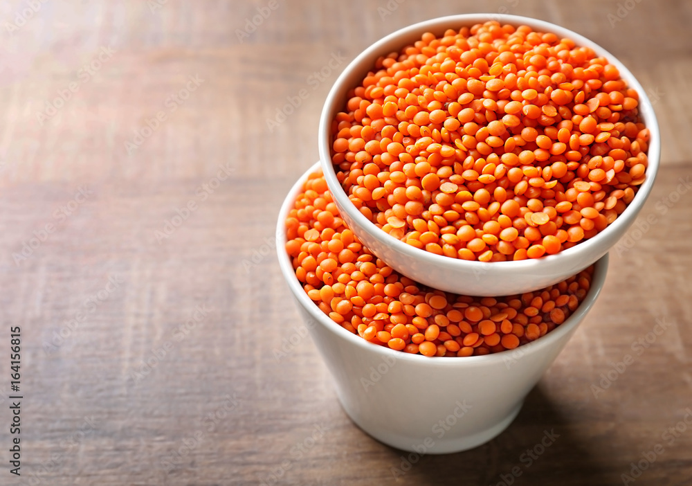 Bowls with red lentils on wooden background