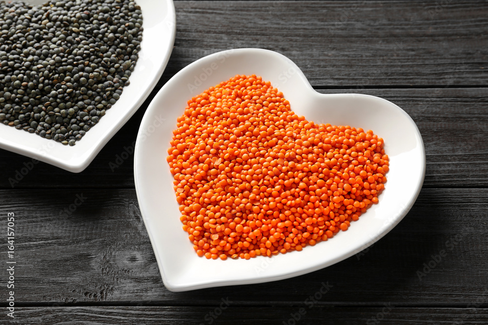 Plates with red and black lentils on wooden background