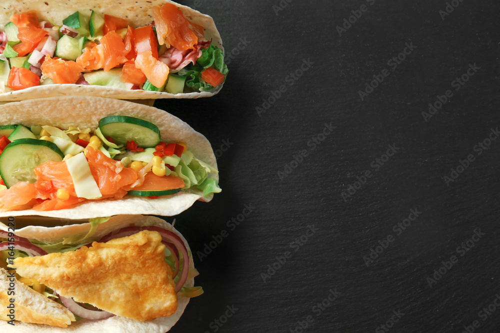 Different tasty fish tacos on dark table