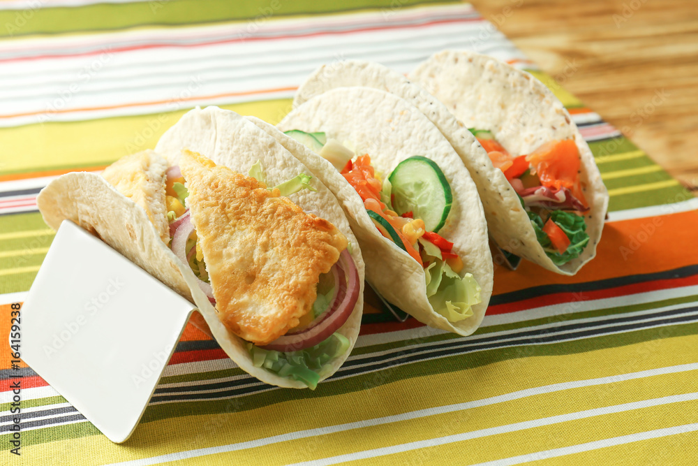Stand with tasty fish tacos on colorful napkin