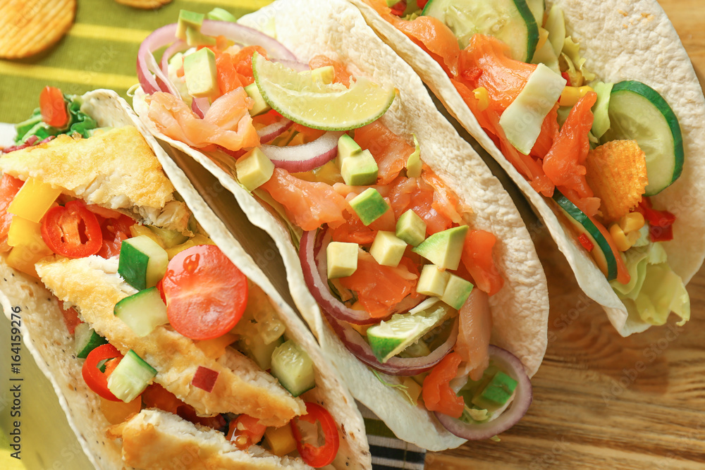 Different tasty fish tacos on wooden background