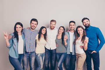 Eight cheerful young people embracing and smiling on the pure backgroung in casual clothes. Ladies are showing two fingers sign