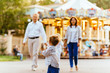 © Iryna - Cute toddler boy running in amusement park with her family on background. Family vacation concept.
