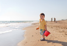Boy Carrying Bucket And Shovel On Beach
