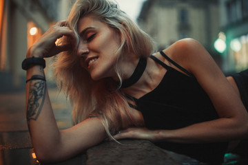 Portrait of young woman lying on wet pavement on city street in evening.