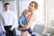 © Nestyda - Sad little child, boy, hugging his mother at home. Family concept. Father in soft focus