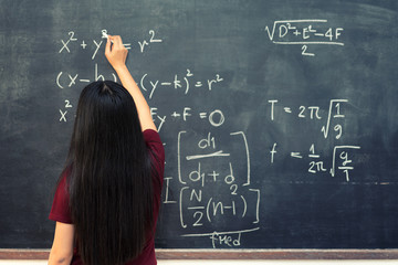 Beautiful Asian student writing on blackboard with chalk in classroom.