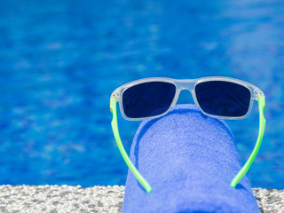 Wall Mural - Sunglesses and blue towel at the side of swimming pool. Vacation, beach, summer travel concept