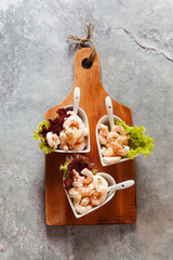 Prawn cocktail  in serving bowls in the form of hearts on a gray background.On a wooden cutting board.close-up