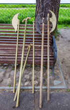 Ancient Lances And Spears Of Wood And Metal Stand Near A Modern Bench In The Public Park
