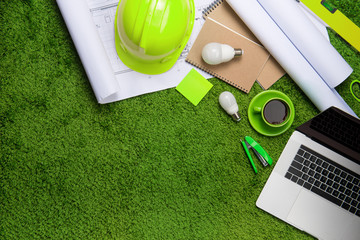 Workplace with helmet, blueprints, laptop and notepad on grass background. Top view with copy space