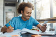 © wayhome.studio  - College student with dark skin and bushy hairstyle smiling happily while reading messages on mobile phone, messaging with his girlfriend online using free internet connection during lunch at cafe