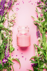 Wall Mural - Natural herbal skin care cosmetic concept. Glass jar with cream or lotion and fresh herbs and flowers on pink background, top view, copy space, vertical.  Beauty, skin and hair care concept