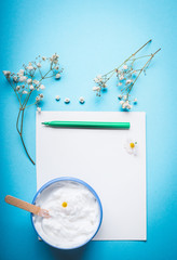 Wall Mural - Jar of cream with flowers and spatula on blank paper with pen for Note or list on blue background. Natural herbal skin care cosmetic concept, top view.  Beauty, skin and hair care concept