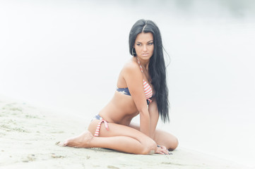 Young beautiful black-haired woman posing on the beach in the water