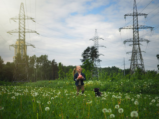 A girl with a dog playing in a field with a ball. Background high-voltage power lines. Summer, warmth, green grass