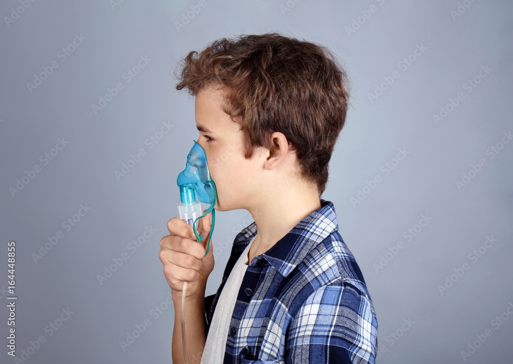Young boy using nebulizer for asthma and respiratory diseases on light background