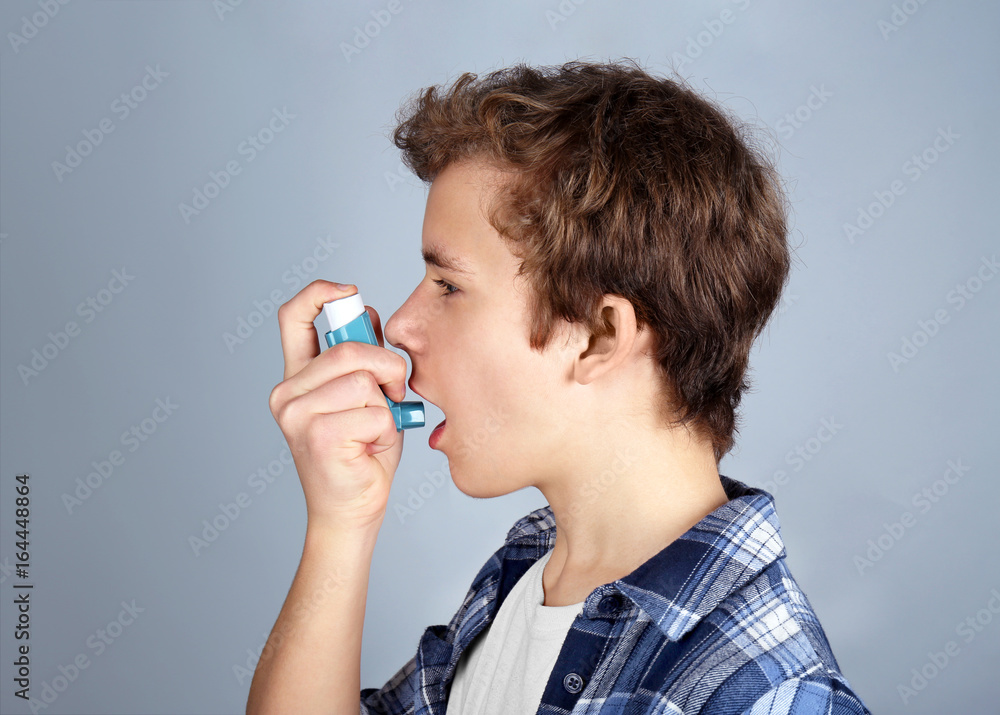 Young boy using inhaler for asthma and respiratory diseases on light background