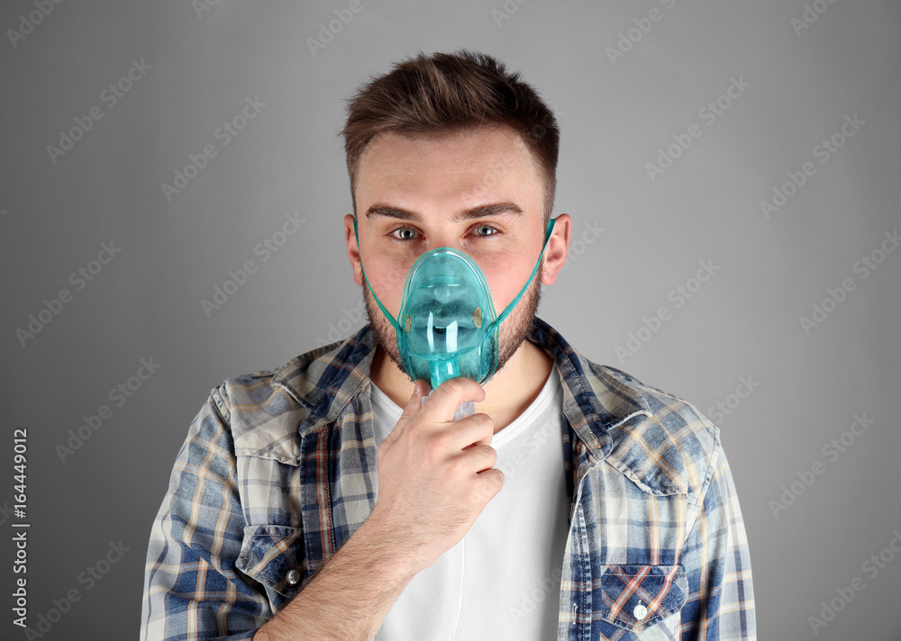 Young man using nebulizer for asthma and respiratory diseases on light background