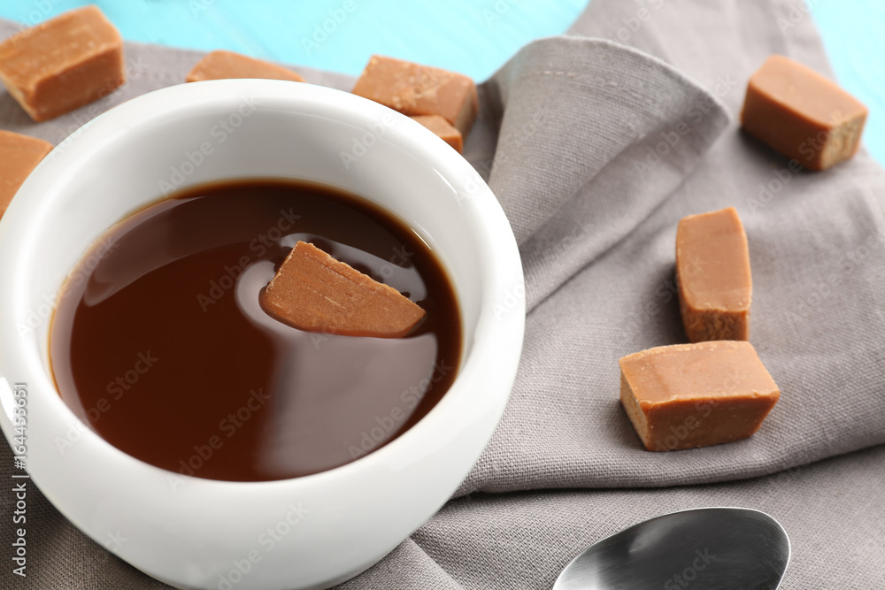 Bowl with caramel sauce and candies on table