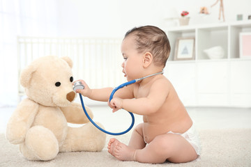 cute little baby with stethoscope and toy bear playing at home. health care concept