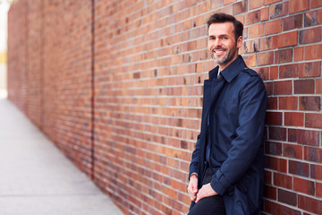 Cheerful confident business manager leaning on brick wall