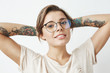 © Cookie Studio - Portrait of beautiful young tattooed girl in glasses smiling looking at camera over white background.