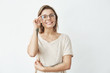 © Cookie Studio - Young pretty girl smiling looking at camera correcting glasses over white background.