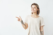 © Cookie Studio - Cheerful young pretty girl smiling looking at camera pointing finger in side over white background.