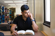 © mdurson - Tired male college student sitting in the library, reading a book, looking tired and drained