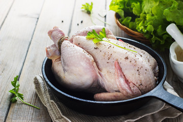 Raw chicken on a cast-iron frying pan on a wooden background